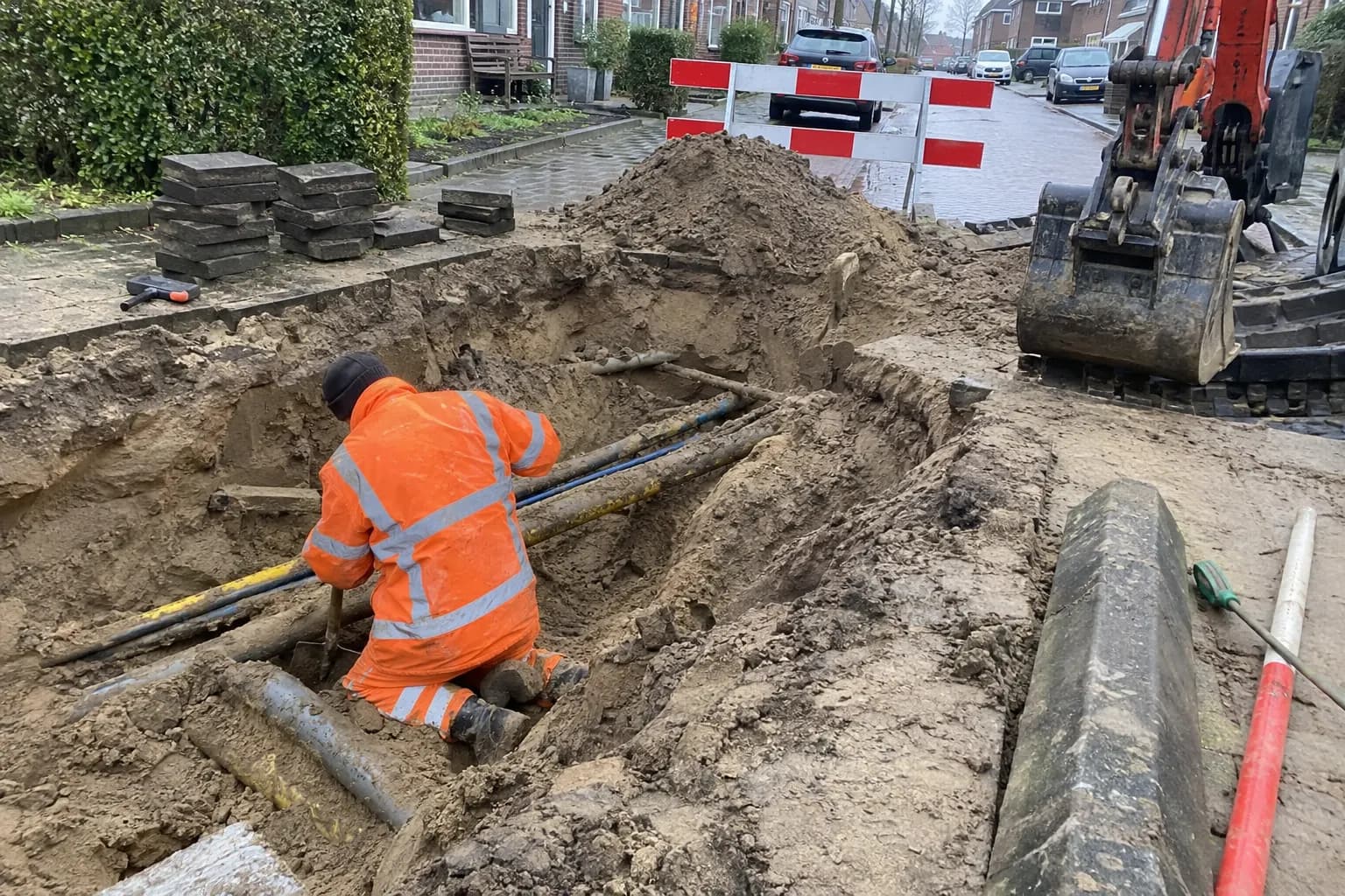 Minigraver graaft een smalle sleuf in een stoep, met opgeslagen grond naast de sleuf